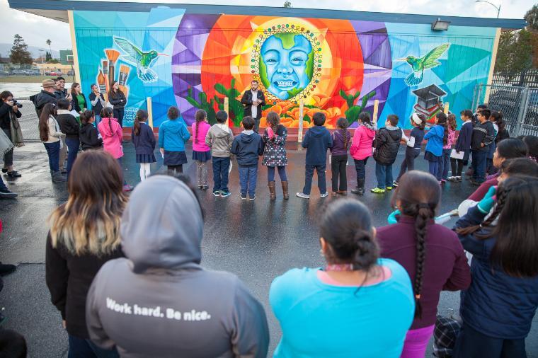 People gathered in front of a colorful mural during a ceremony.