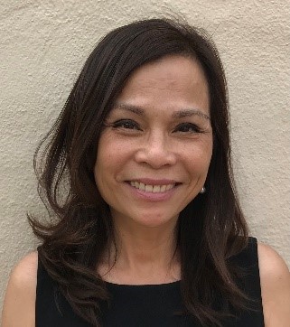 A person smiling in front of a beige wall background.