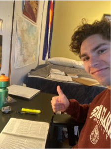 Person smiling and giving a thumbs-up while sitting at a desk with study materials.