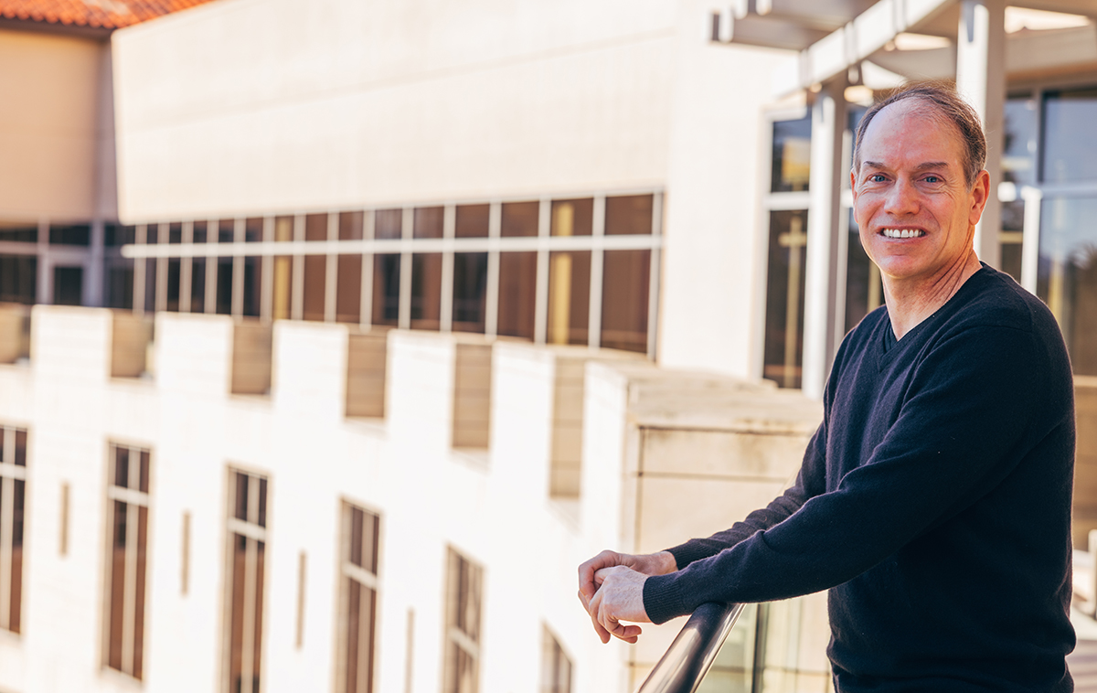 Kris Mitchener standing on the balcony of Lucas Hall with the building curving around to the left in the background.