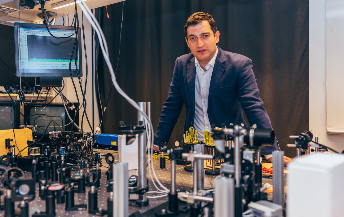 A man in a blue sport coat leaning over a table of laser equipment