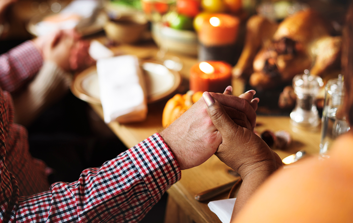 A man and woman's hand come together in prayer at Thanksgiving dinner table.