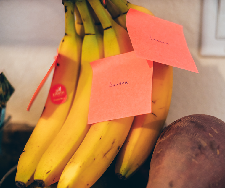 A bunch of bananas sit on a kitchen counter, with three stickie notes says 
