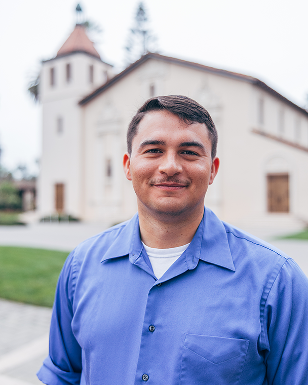 Close-up of a young man in a casual blue button down with the Mission Church in the background.