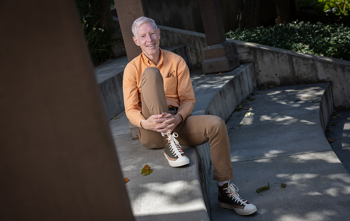 A man in an orange shirt and green sneakers sits on a cement exterior stair.