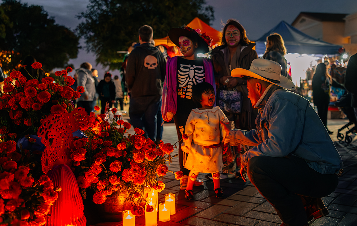 A Latino family stands by a candlelit altar outside at night.
