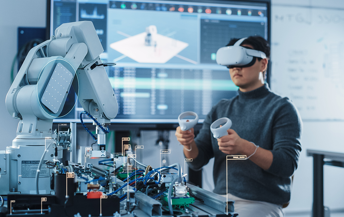A man wearing a VR headset uses hand controllers to control a robot in a lab setting.
