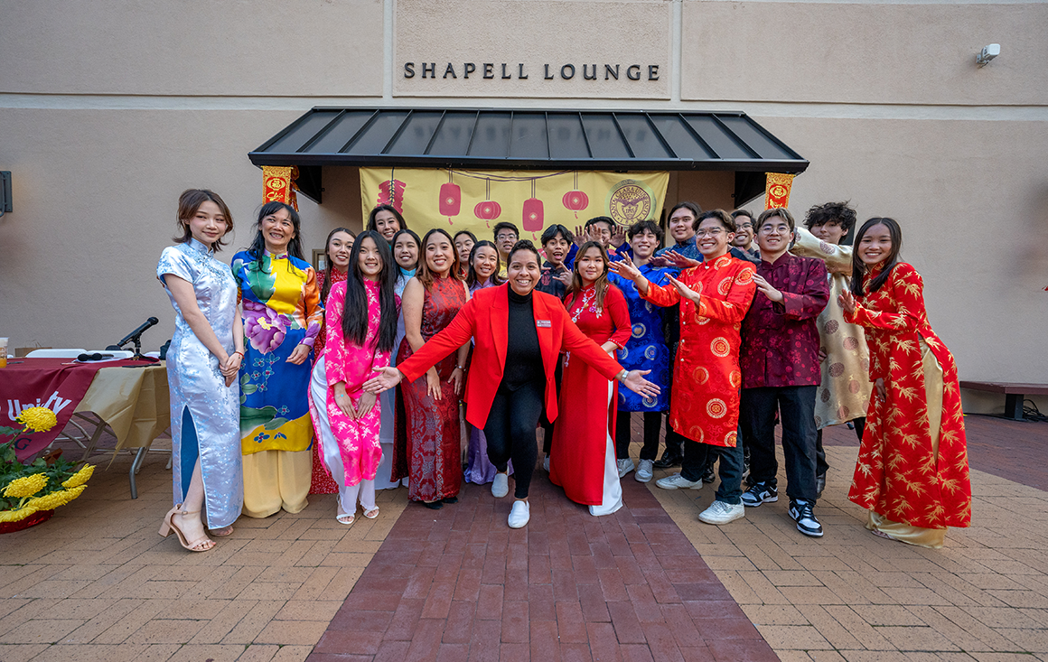 A Black Latina woman stands amidst several Asian students wearing tradition Lunar New Year attire.