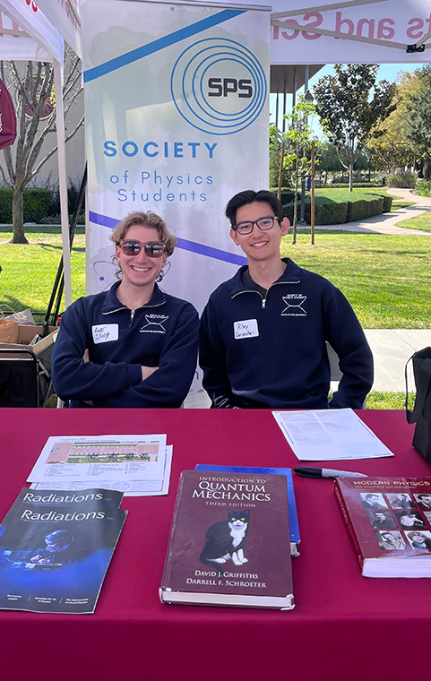Two male students sit at a tabling event advertising the 