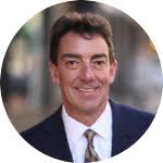 A person smiling in a business suit with a blurred background.