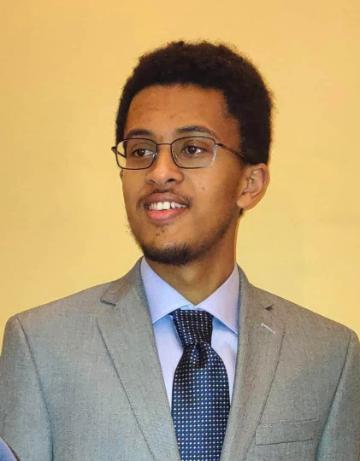 A person in a suit and tie smiling against a plain background.