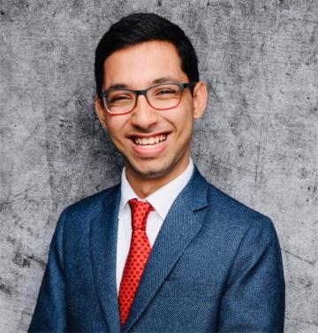 A person in a suit and glasses smiling.