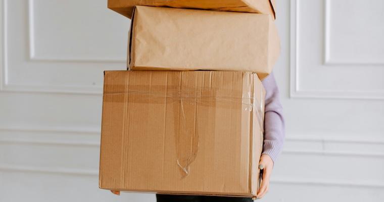 A person holding a stack of brown boxes 