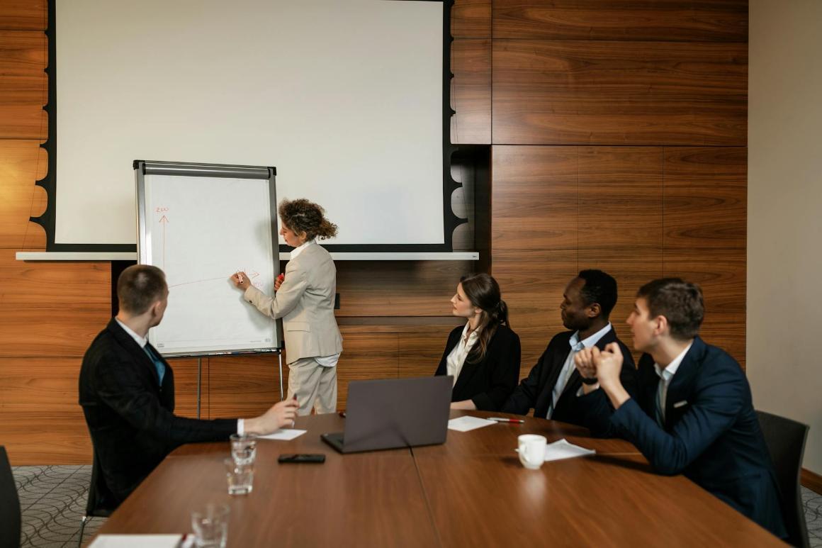 Business professionals watch colleague write on a whiteboard