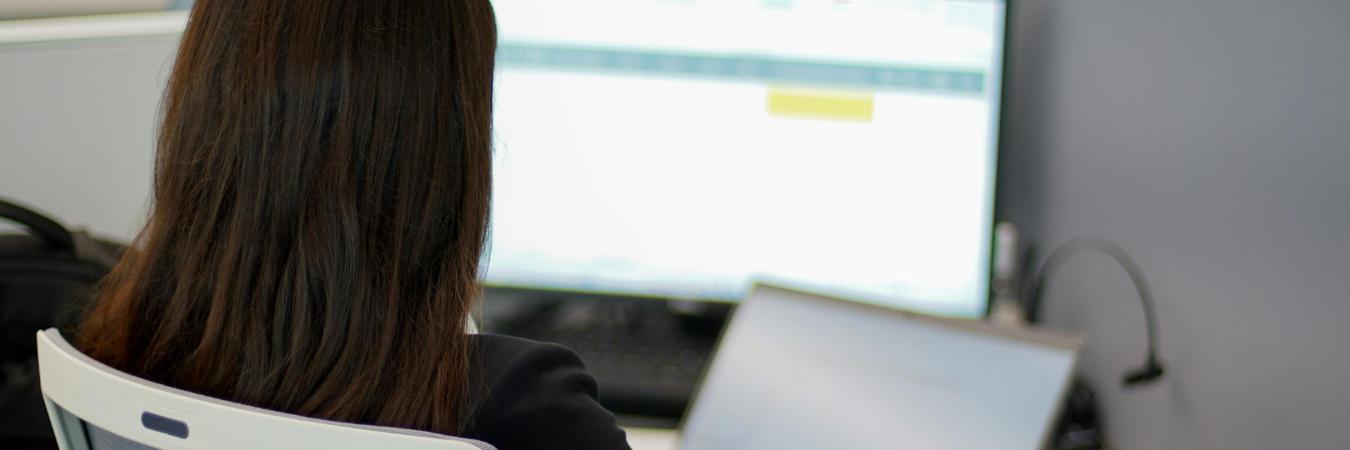 Businesswoman looking at spreadsheets on laptop and monitor