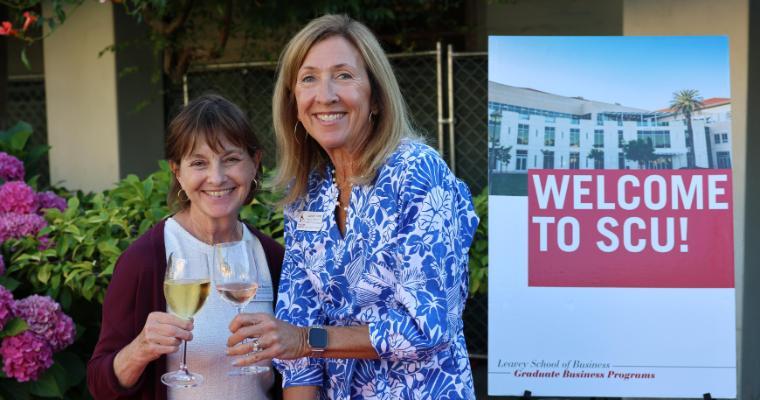 Two admissions advisors toast with wine glasses outdoors at graduate business new student welcome.