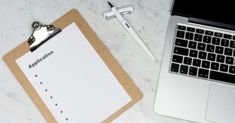 White paper reading 'application' on brown folder beside silver laptop computer