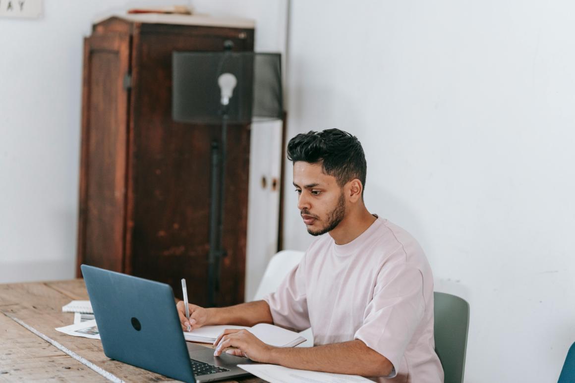 Student working on laptop while taking notes by hand