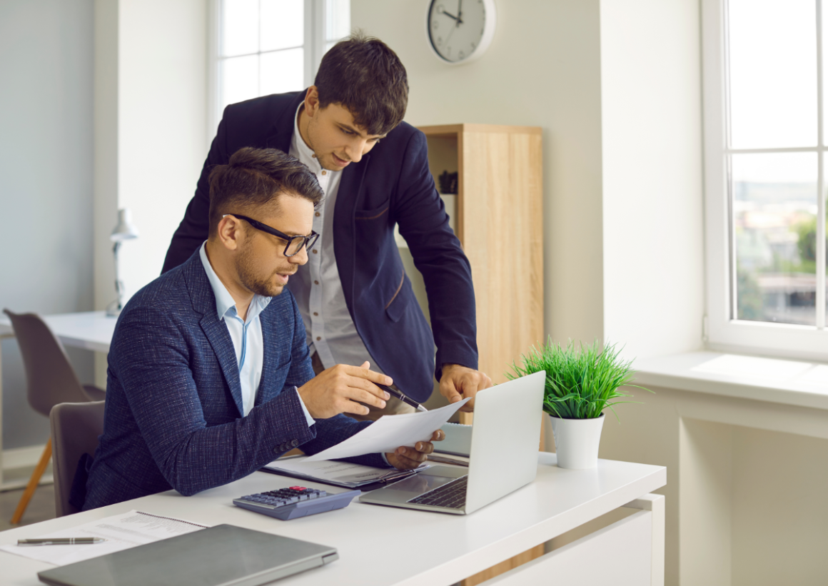 Finance professionals discussing paper with open laptop