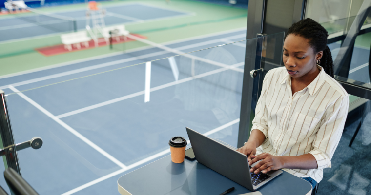 Business professional working on laptop with tennis courts in the background image link to article