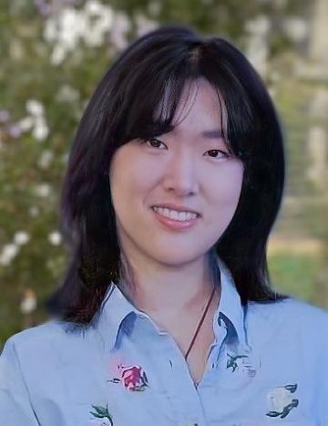 A person wearing a blue shirt, smiling, with a nature background.