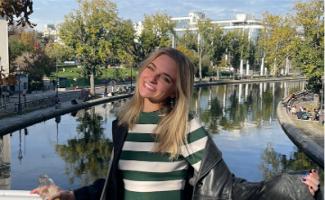 Person smiling by a river with trees in the background.