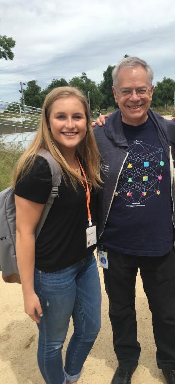 Two individuals standing outdoors, smiling at the camera.