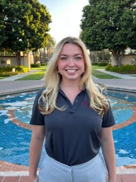 A person standing outside near a fountain, wearing a dark shirt.