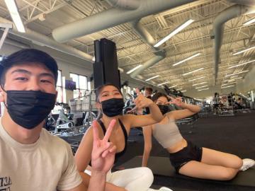 Three people wearing masks posing together at a gym.