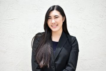 A person in a black blazer, smiling against a white background.