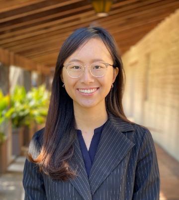 A person wearing glasses and a black shirt, smiling outdoors.