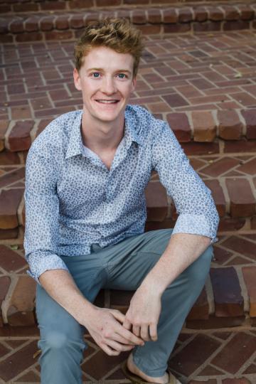 A person sitting on brick steps, smiling, titled 'Cole Normandin'.