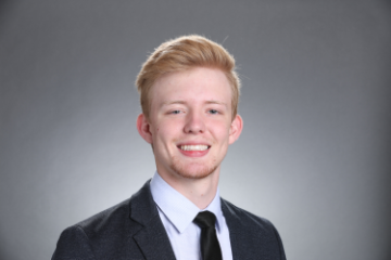 A person smiling in a professional headshot against a gray background.