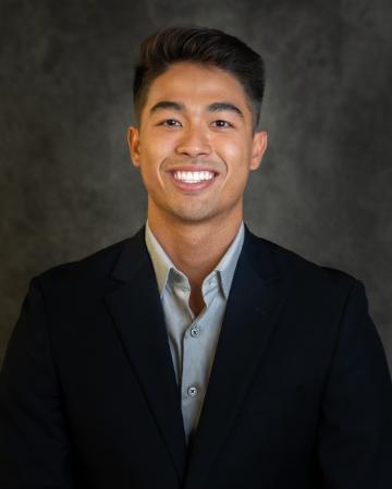 A smiling person in a suit against a dark background.