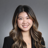 A person smiling in business attire with a gray background. 