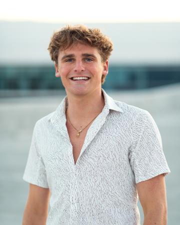 A person wearing a white shirt smiling near a body of water.