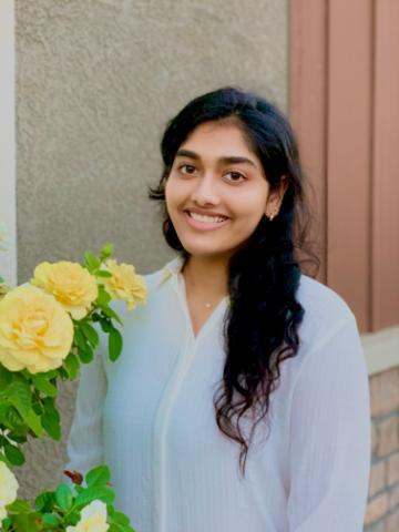 A person smiling next to yellow flowers.