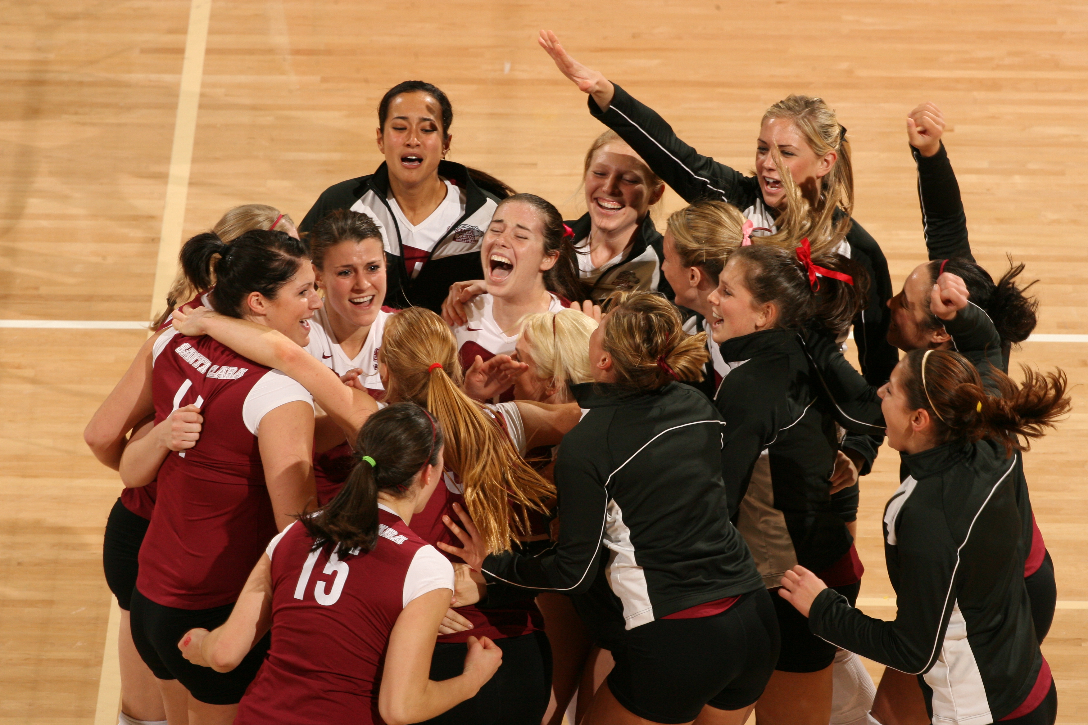 The women's volleyball team gathers in a celebratory huddle