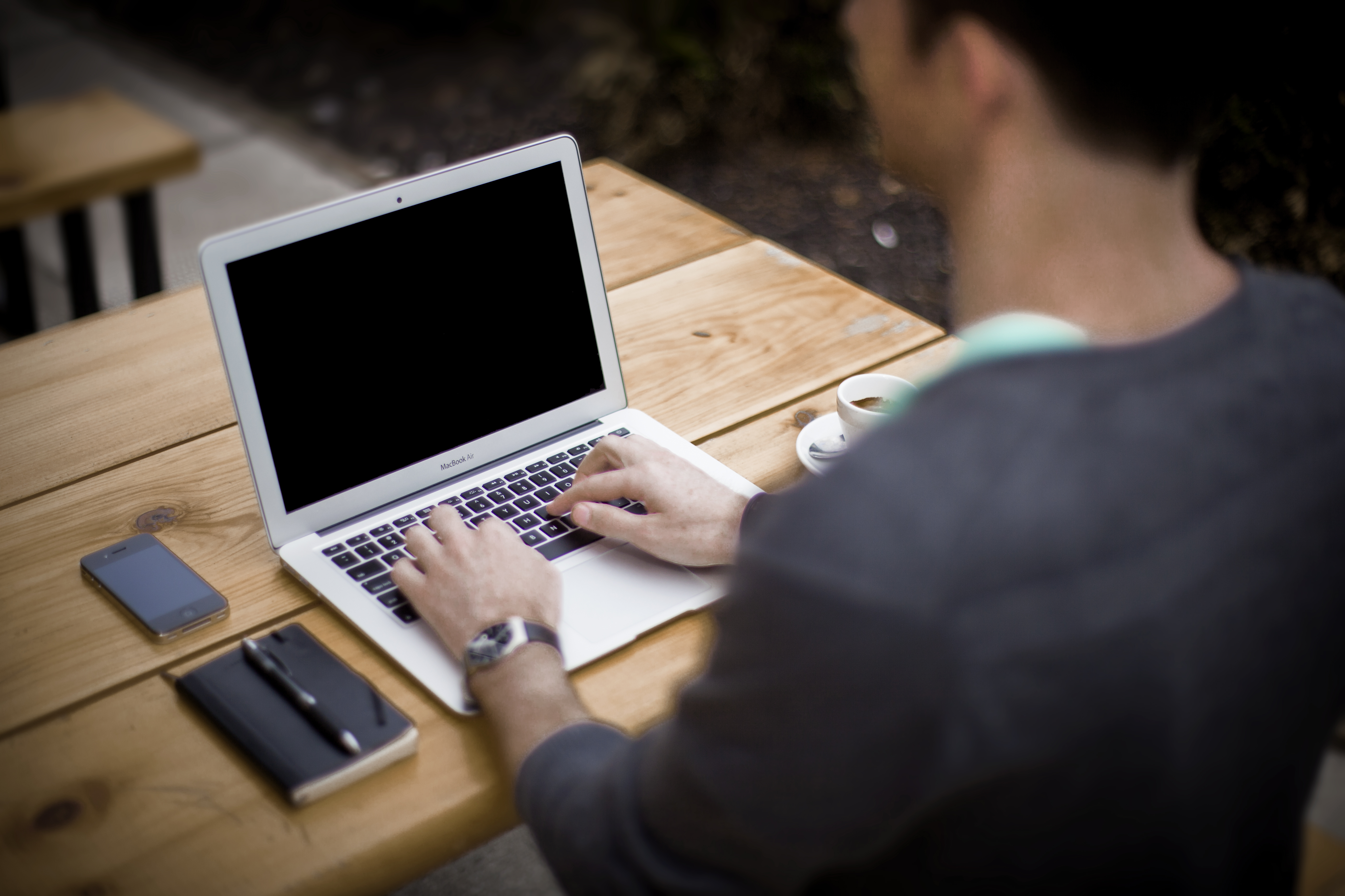 Person working on a laptop with a smartphone and pen nearby.