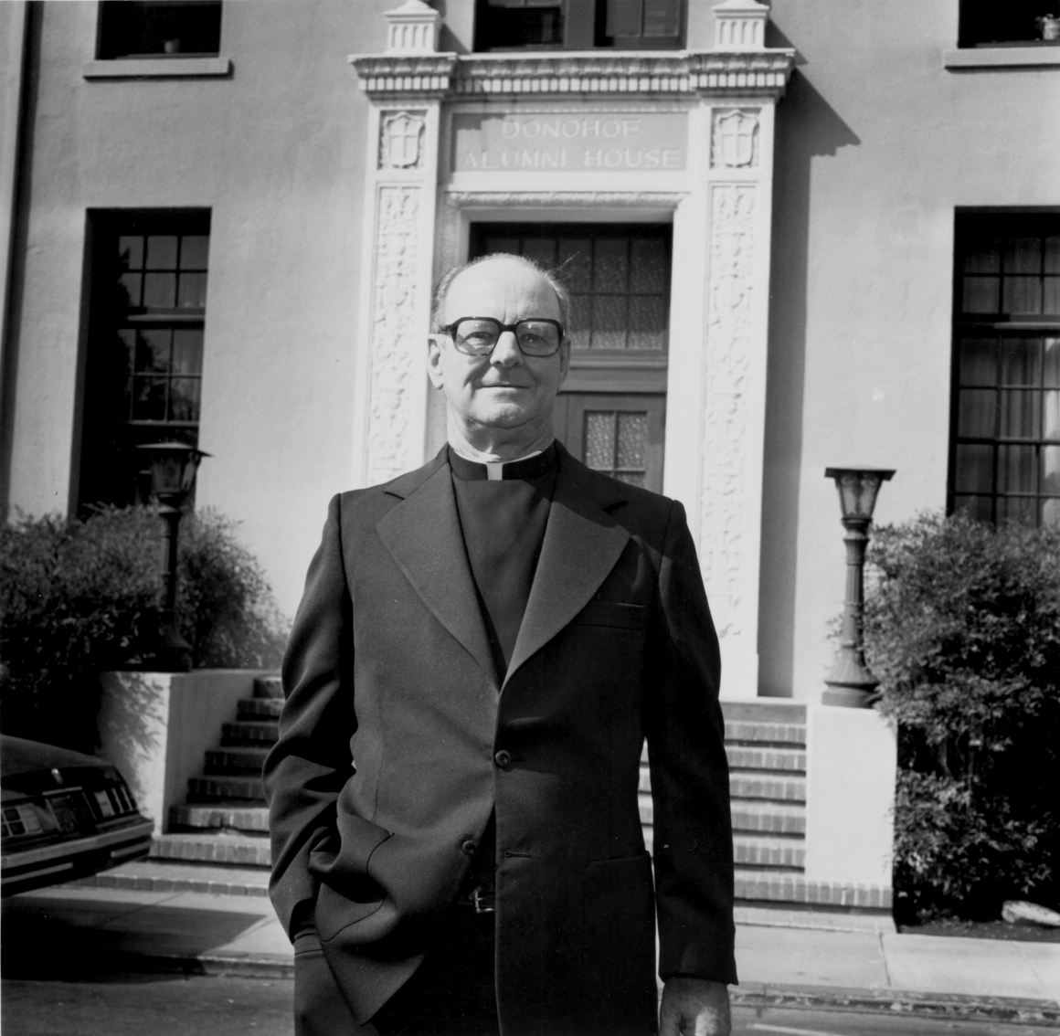 A Jesuit priest standing in front of Donohoe Alumni House at Santa Clara University.