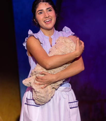 A young woman singing on stage while holding a swaddled baby.