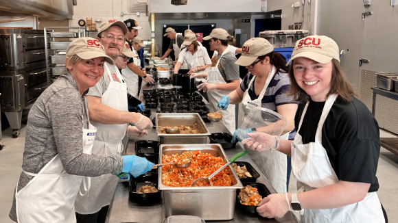 A group of smiling people on both sides of a food preparation line at a service project. 