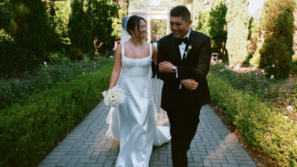 A smiling, happy bride and groom walking on a brick pathway in a green garden.