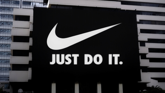 A black billboard with a white Nike brand swoosh and white text underneath, reading
