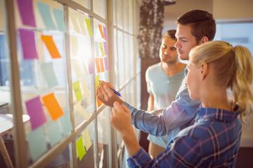 People discussing colorful sticky notes on a window, brainstorming and problem-solving.