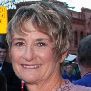 A smiling person with short hair in a formal outfit outdoors.