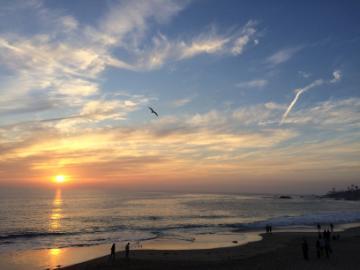 Sunset at Laguna Beach with scattered clouds and distant people near shoreline.