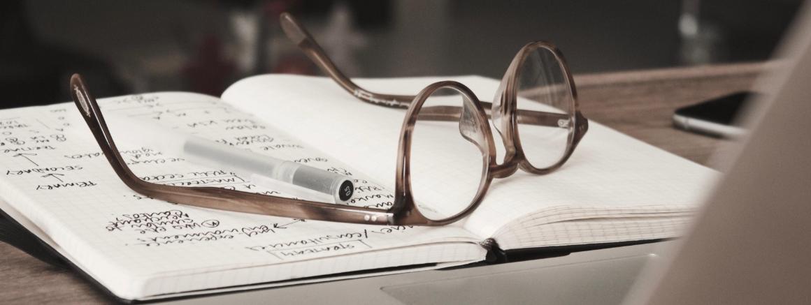 Eyeglasses on an open notebook next to a laptop