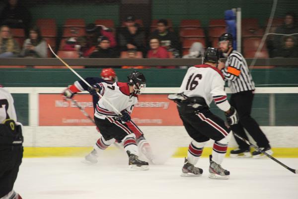 Two men's ice hockey players competing near a referee on the rink.