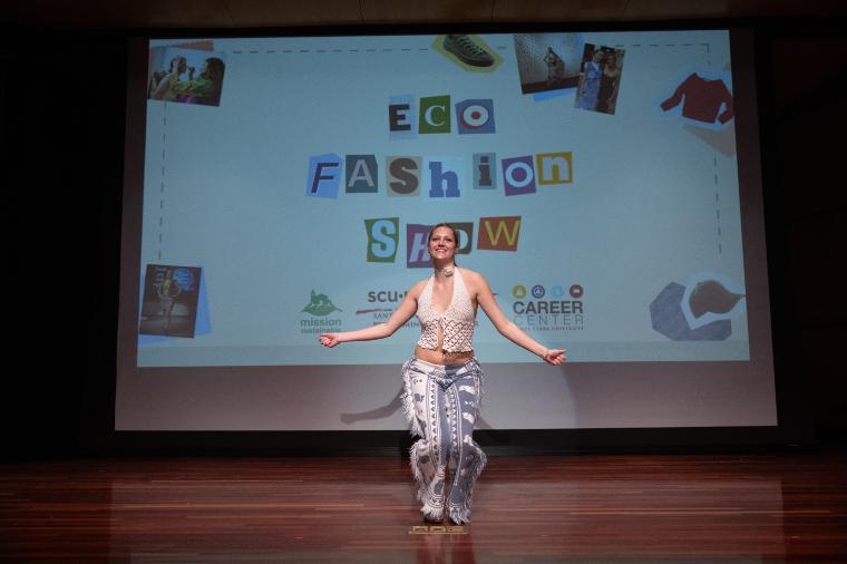 Female model with arms outstretched in front a screen that says EcoFashion Show